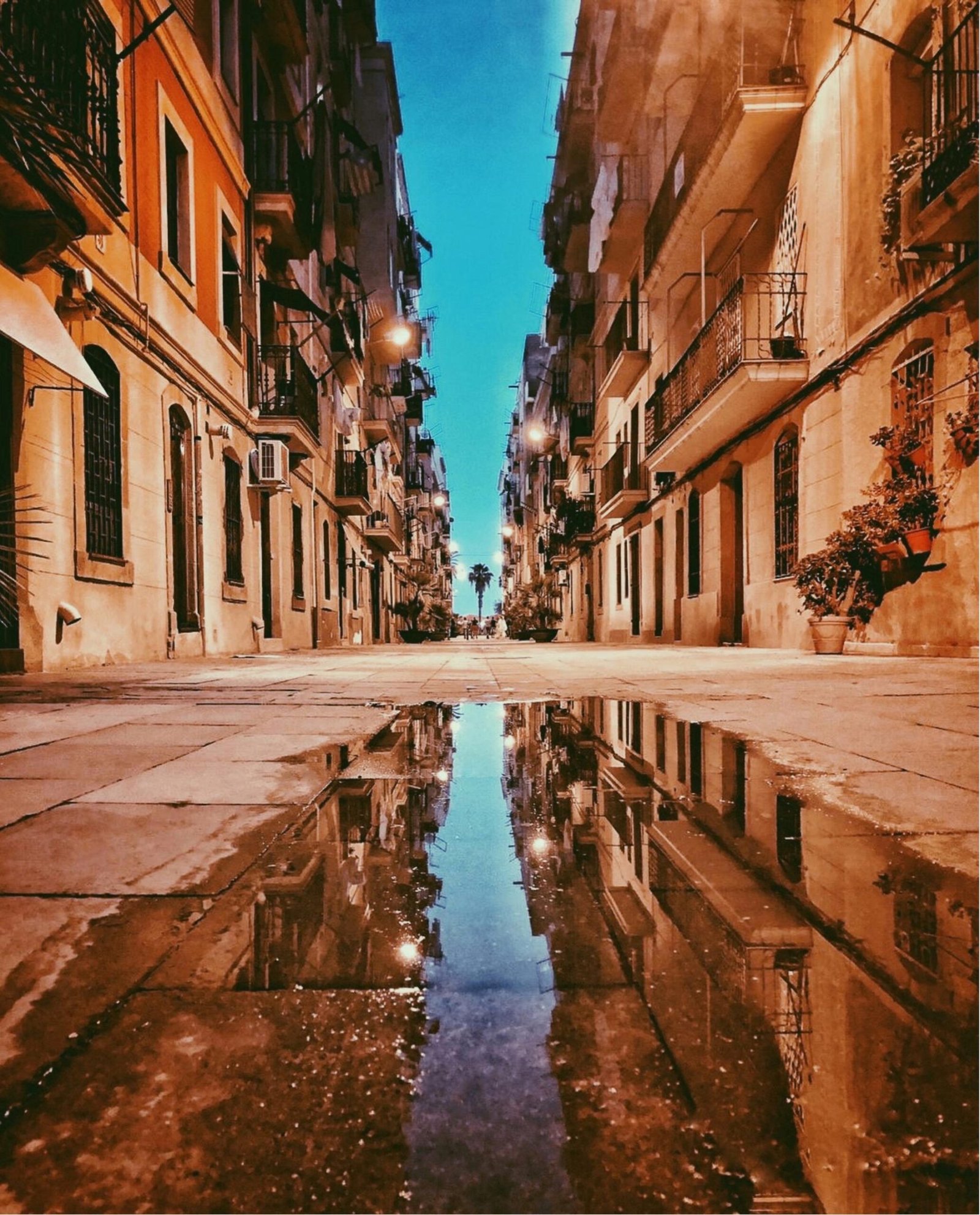 Narrow street in El Born, Barcelona at dusk with historic buildings and reflections on wet pavement